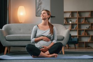 Sitting on the yoga mat. Beautiful pregnant woman is indoors at home